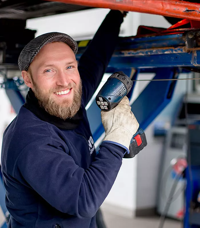 Ein Kfz-Prüfingenieur steht an einer Hebebühne und prüft ein Fahrzeug